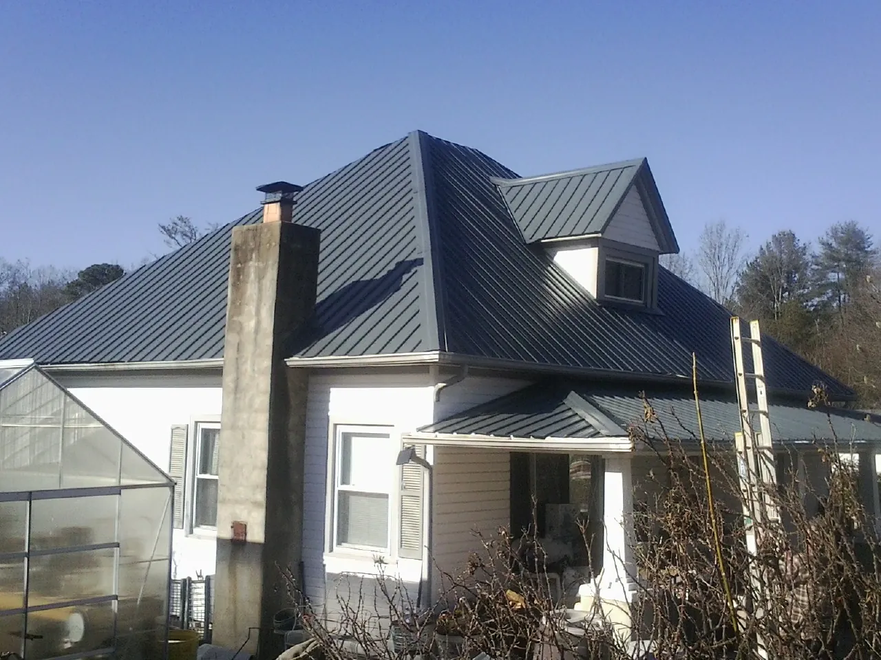 Dark blue standing seam metal roof on a white farmhouse with dormer — Slate & Tile Roof Repair by Roofing Brothers in Ramey