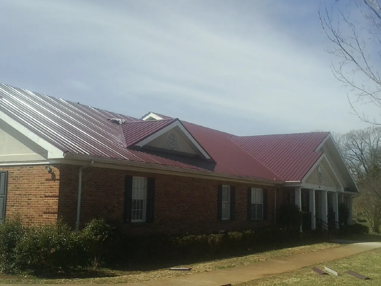 Red metal roof with gabled entries on a long brick building, from a Hail Damage Roof Repair job in Ramey