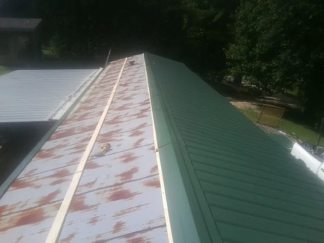 Old rusted panels beside newly installed green metal roofing — Wind Damage Roof Repair by Roofing Brothers in Ramey