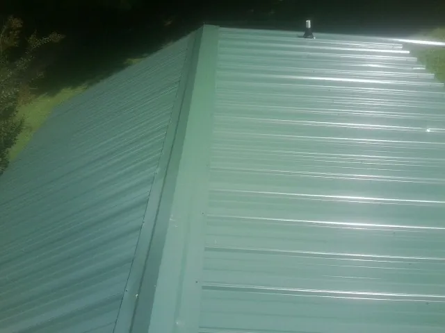 New green metal panels meeting at the ridge of a roof — Flat Roof Repair work by our crew in Ramey
