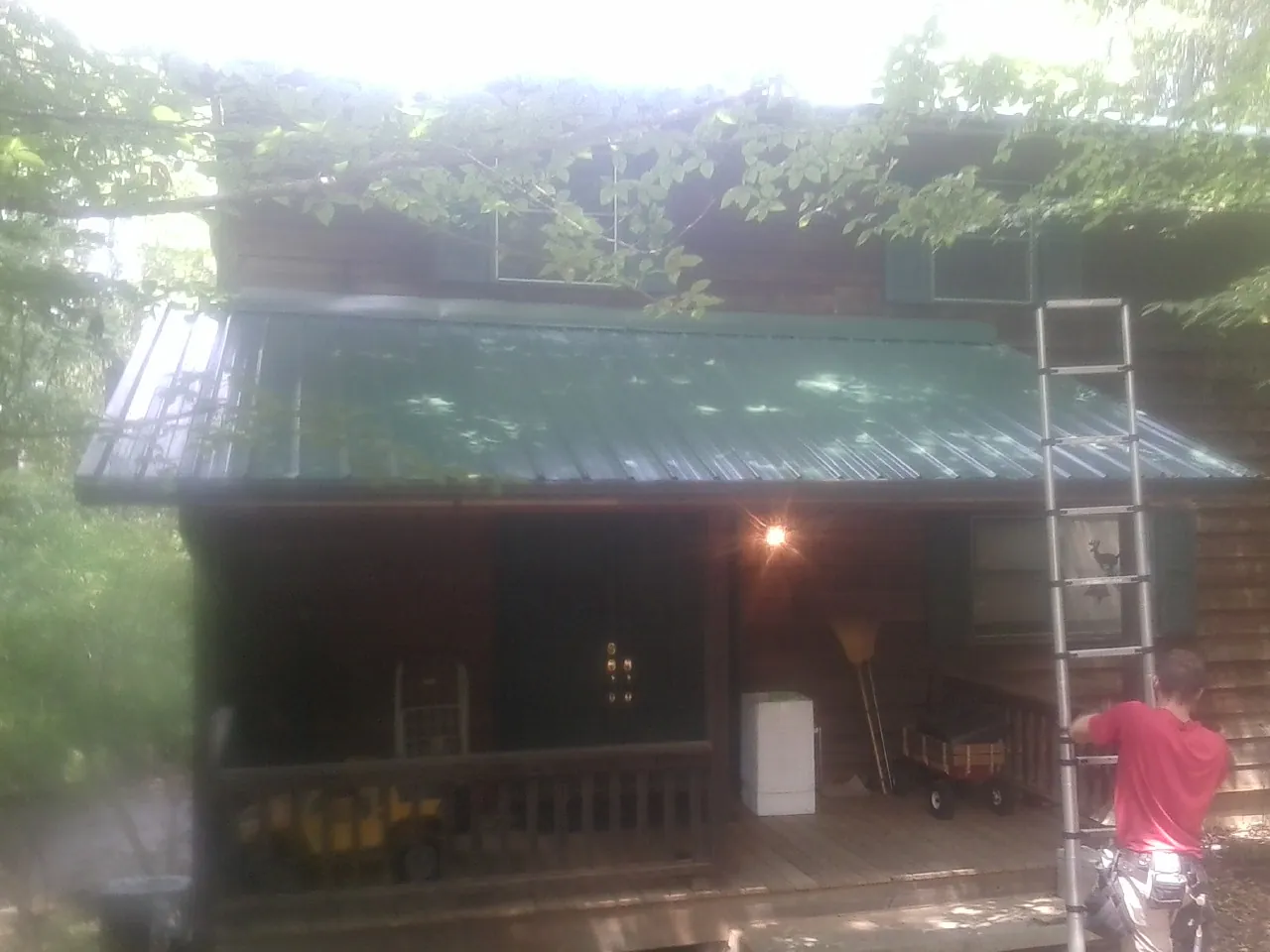 Worker on a ladder at the green porch roof of a wooded cabin in Ramey