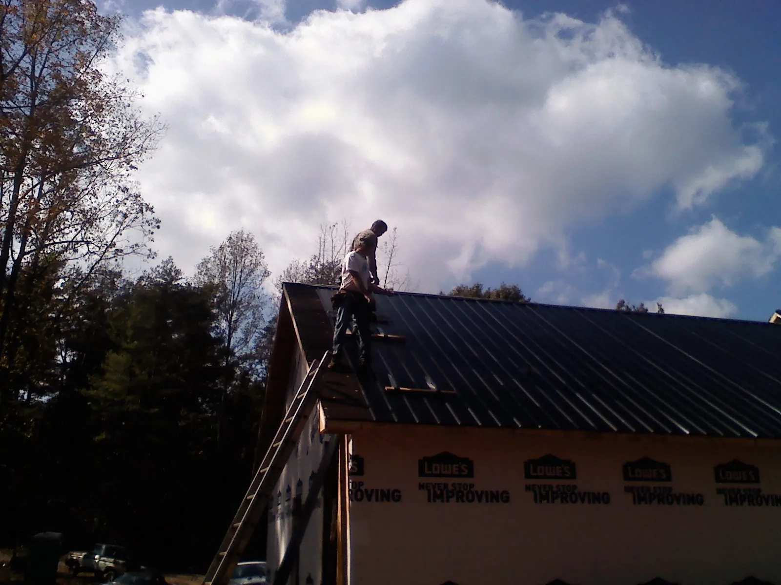 Roofer fastening dark metal panels high against a cloudy sky, from a Roof Inspection job in Ramey