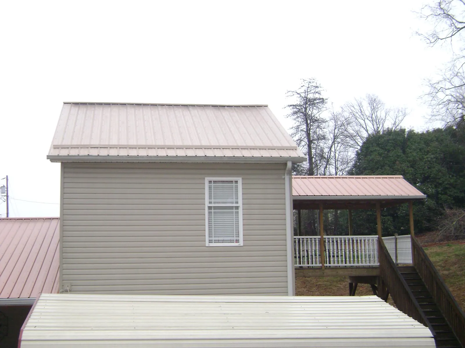 Tan metal roofs on a two story addition and attached porch, from a Roof Replacement job in Ramey